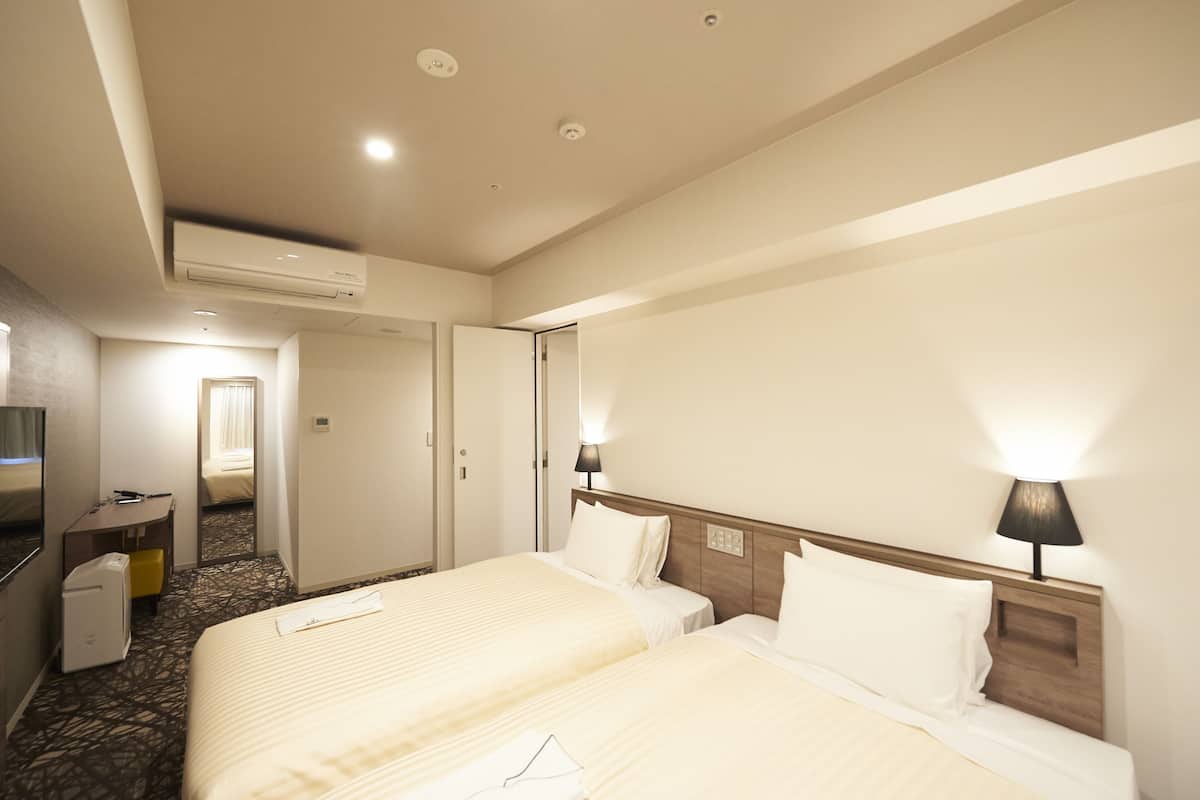 A hotel room with two beds, a desk, a chair, and a television.