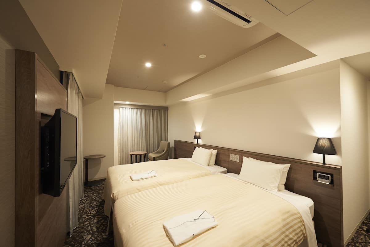 A hotel room with two beds, a TV, a desk, and a chair.