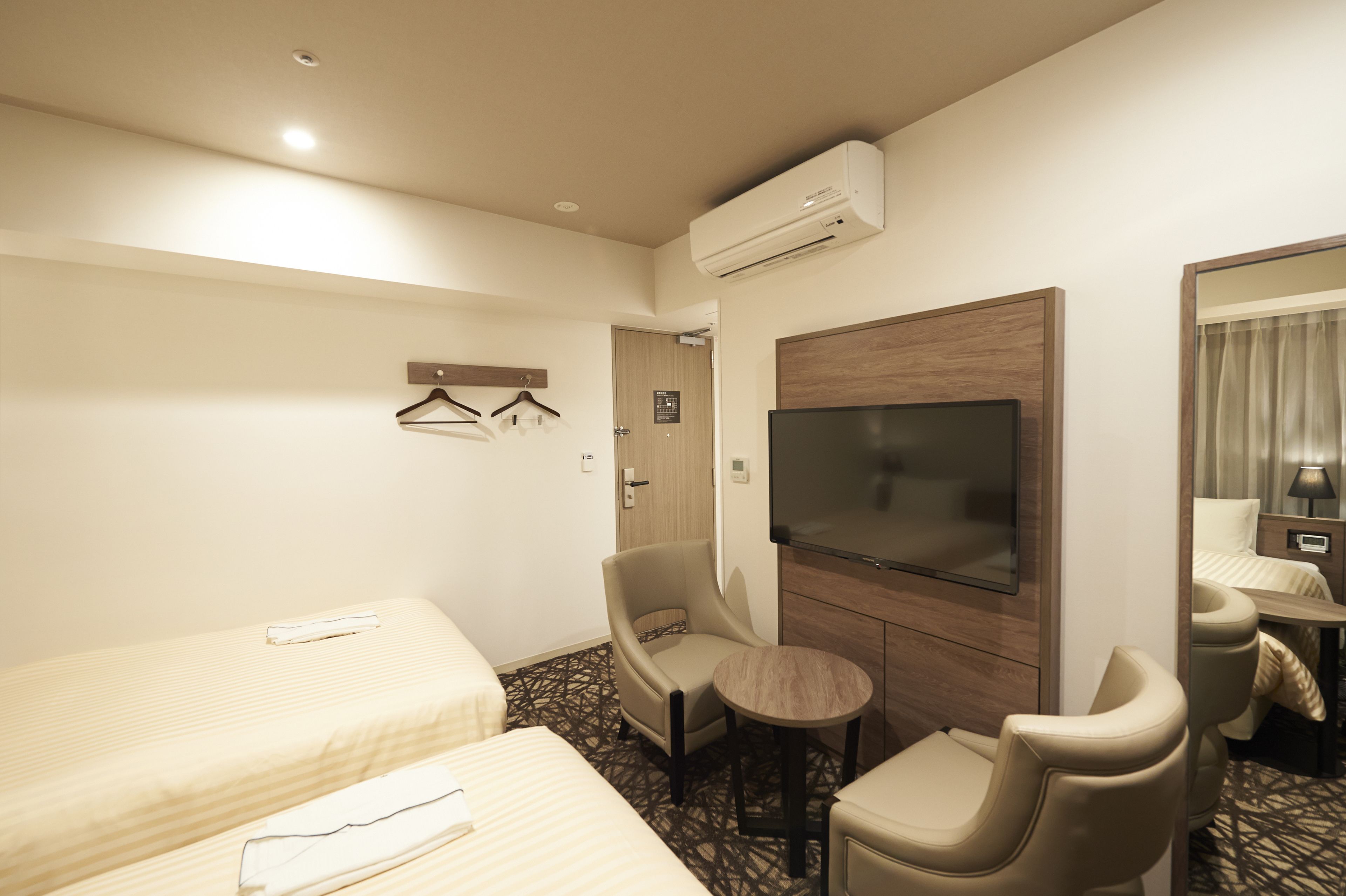 A hotel room with two beds, a TV, a chair, a small table, and a mirror.