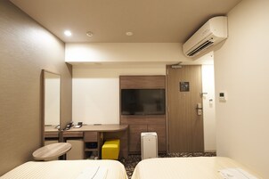 A hotel room with two beds, a desk, a chair, a TV, and an air conditioning unit.