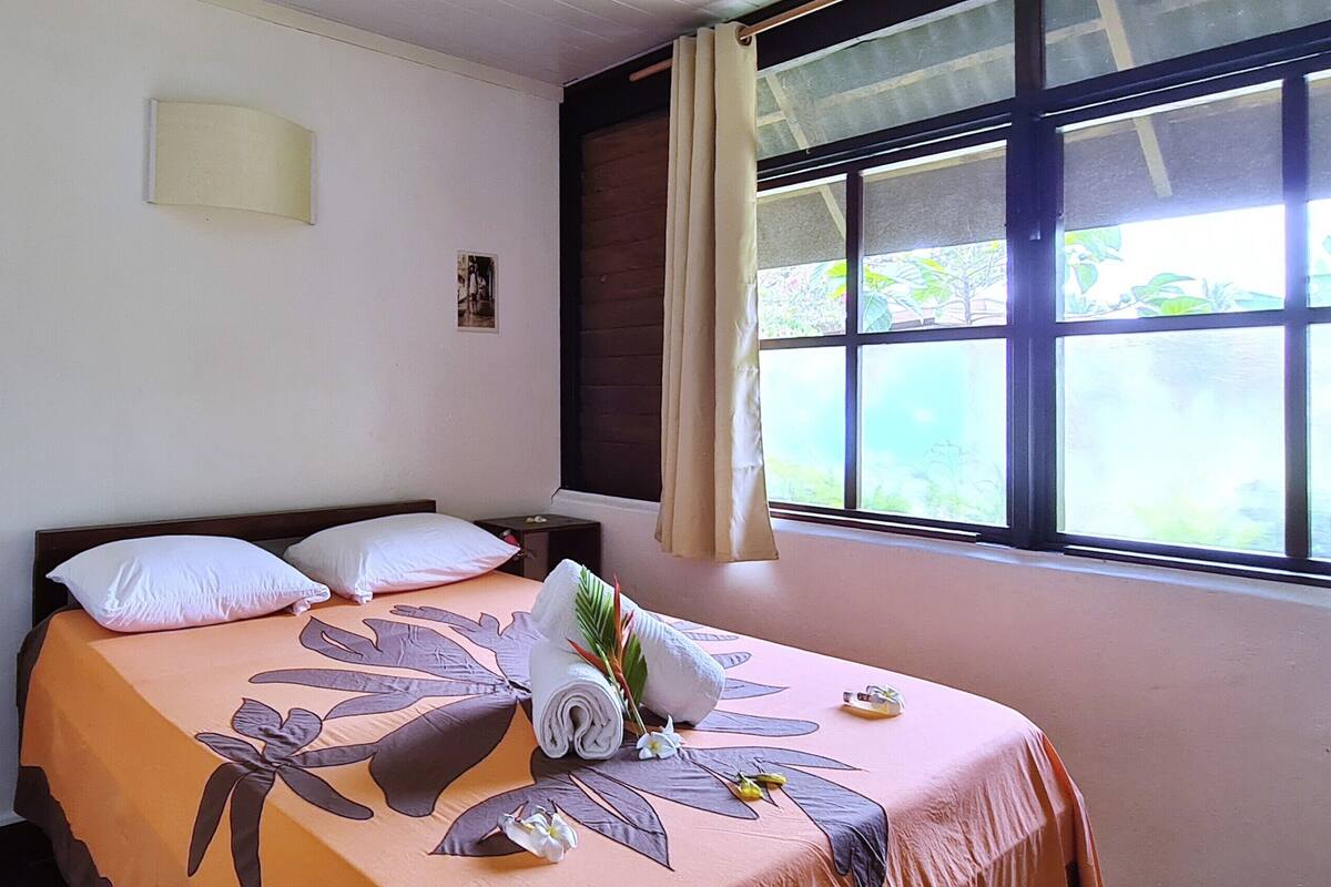 A neatly made bed with a floral bedspread, a small bedside table, and a window with curtains.
