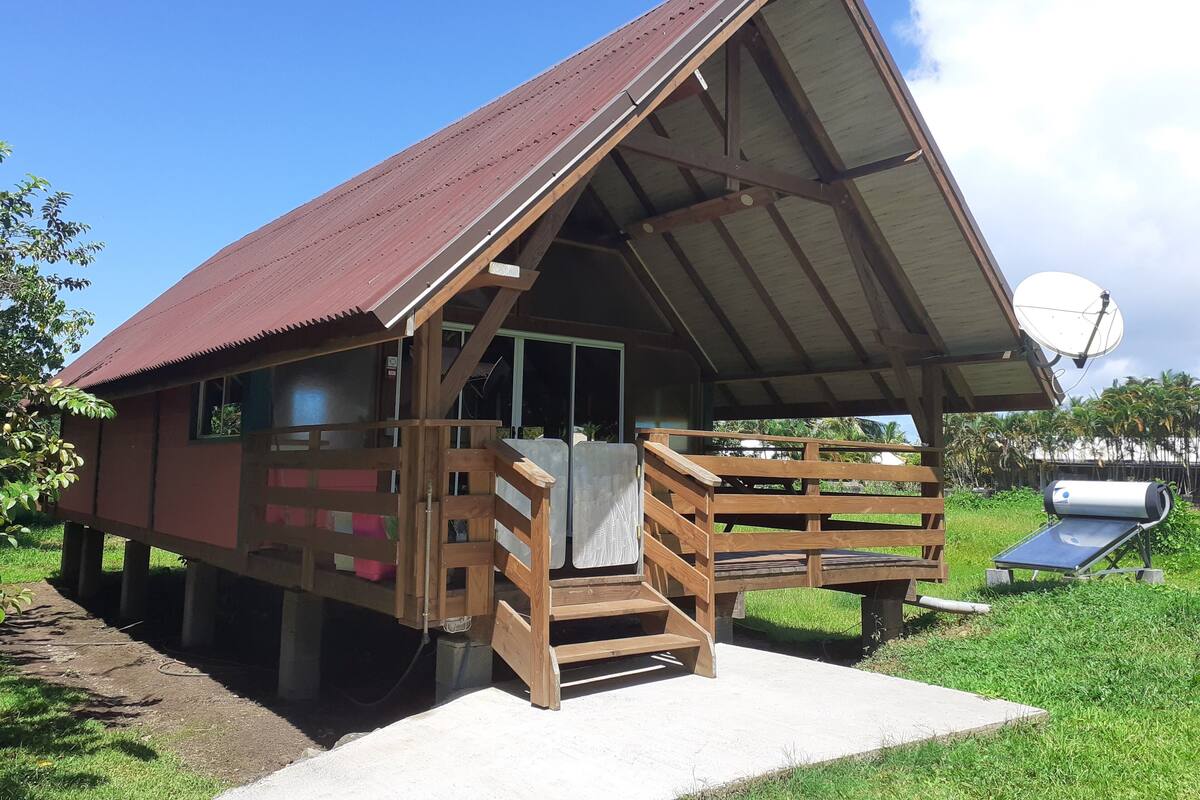A small, single-story wooden cabin with a sloped metal roof, a porch with a wooden railing, and a satellite dish.