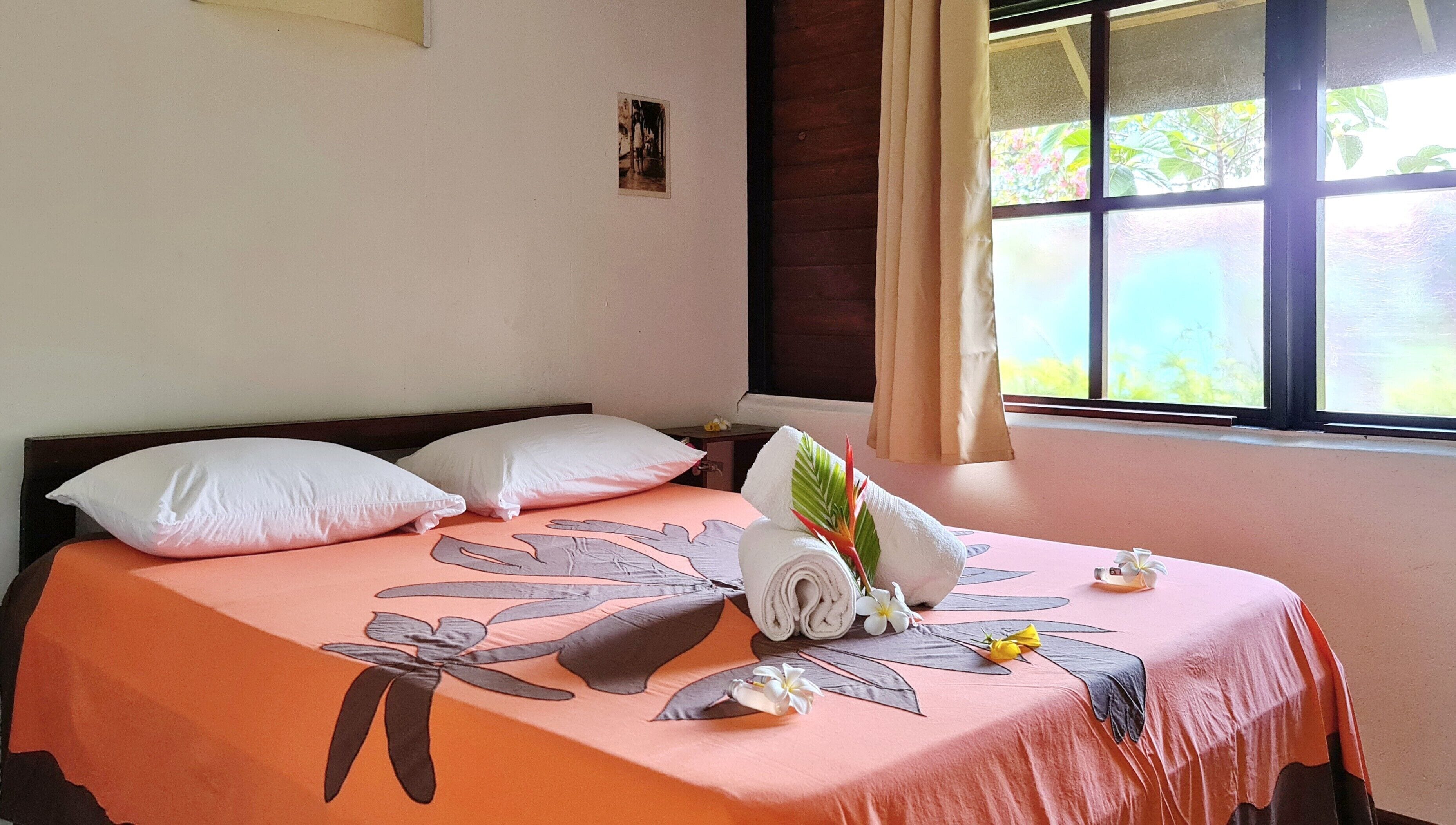 A neatly made bed with a floral bedspread, pillows, and a rolled towel.