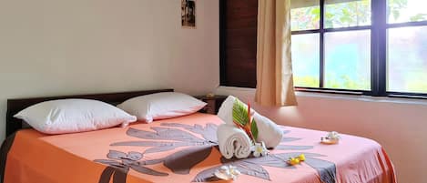 A neatly made bed with a floral bedspread, pillows, and a rolled towel.