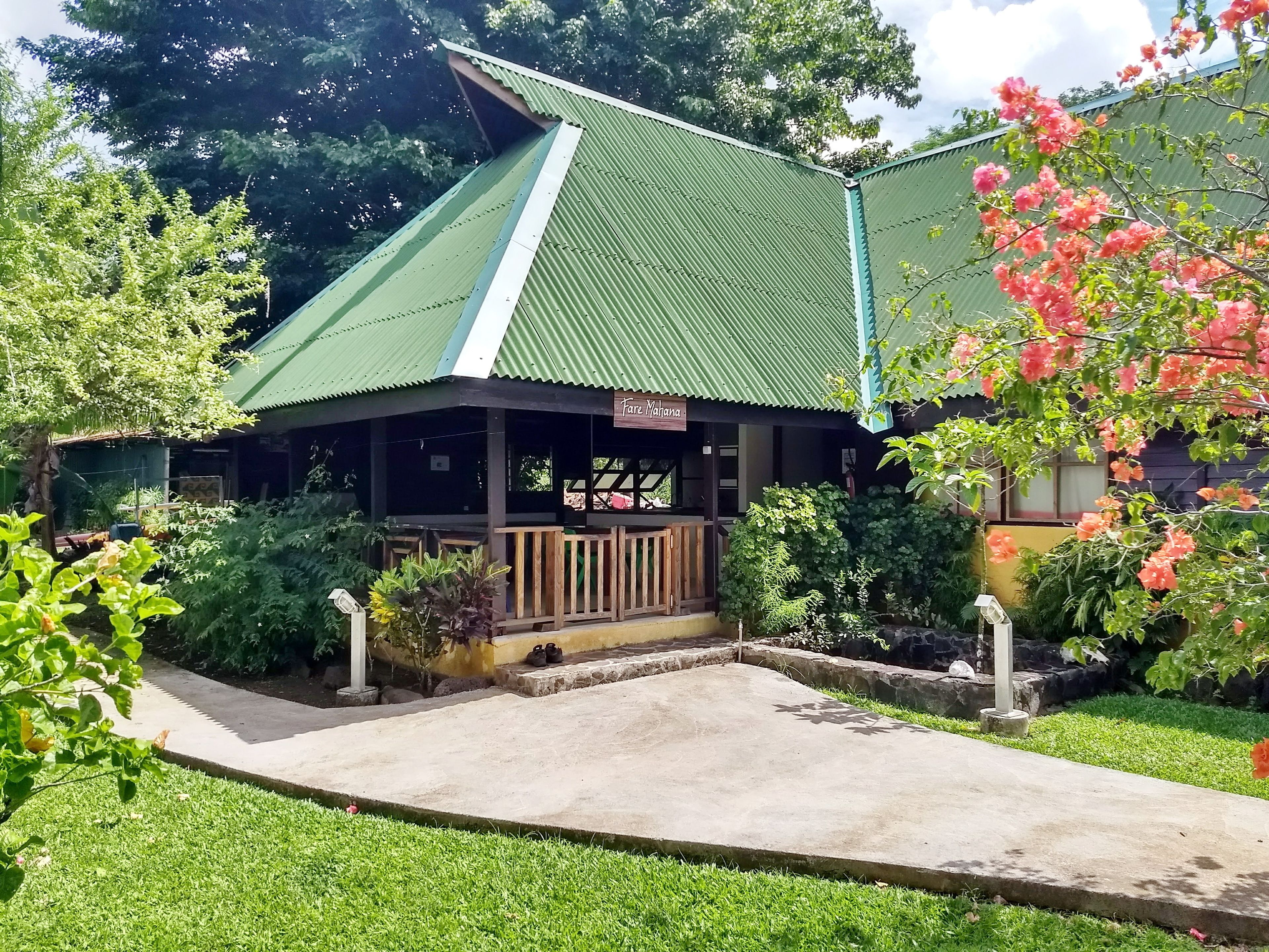 A rustic building with a green roof, a wooden porch, and a sign that reads "Fure Mahana".