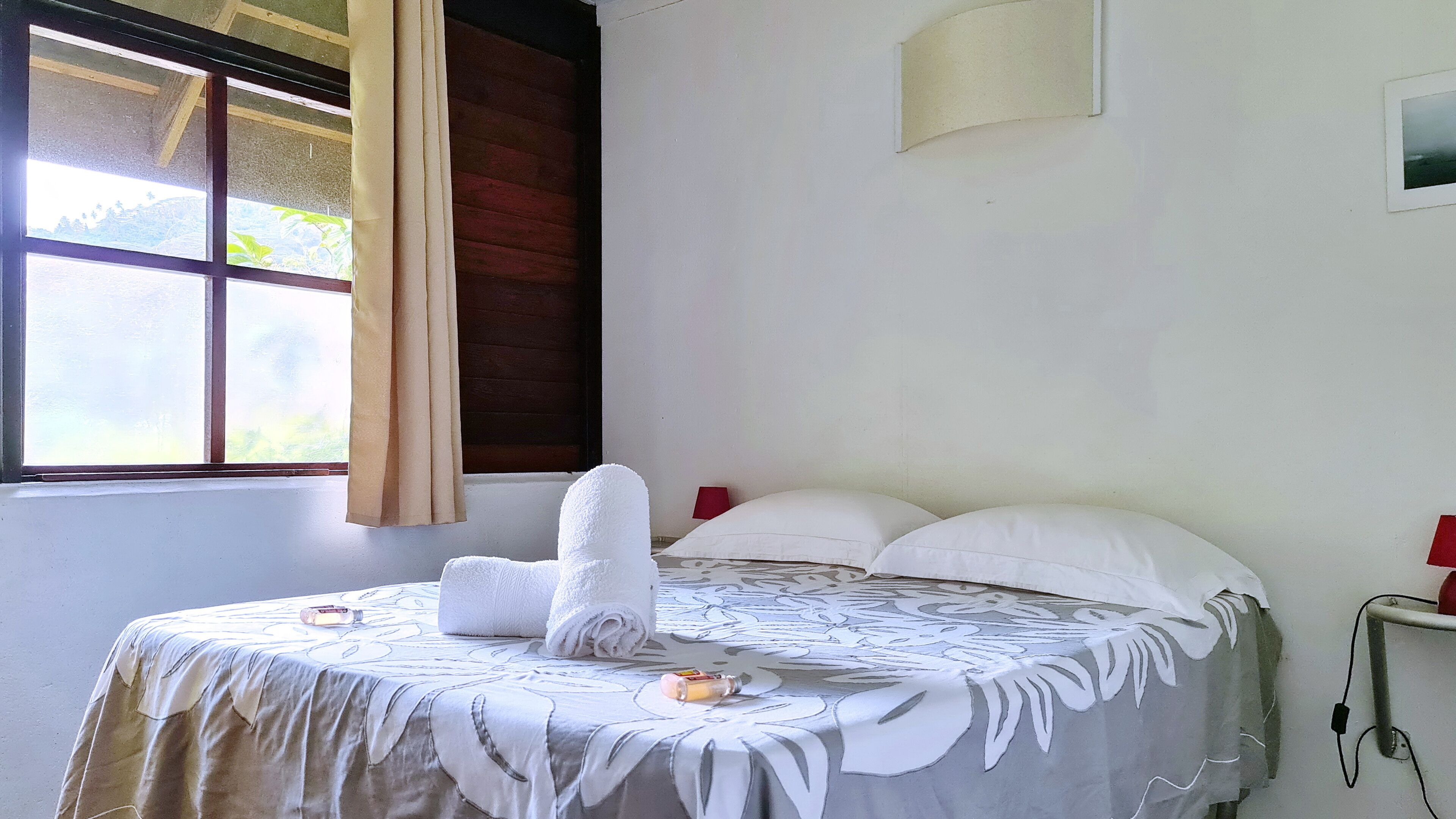A neatly made bed with a white duvet, a rolled-up towel, and a bottle of lotion on the bed.