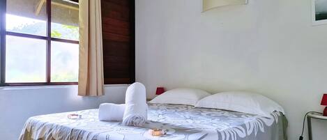 A neatly made bed with a white duvet, a rolled-up towel, and a bottle of lotion on the bed.
