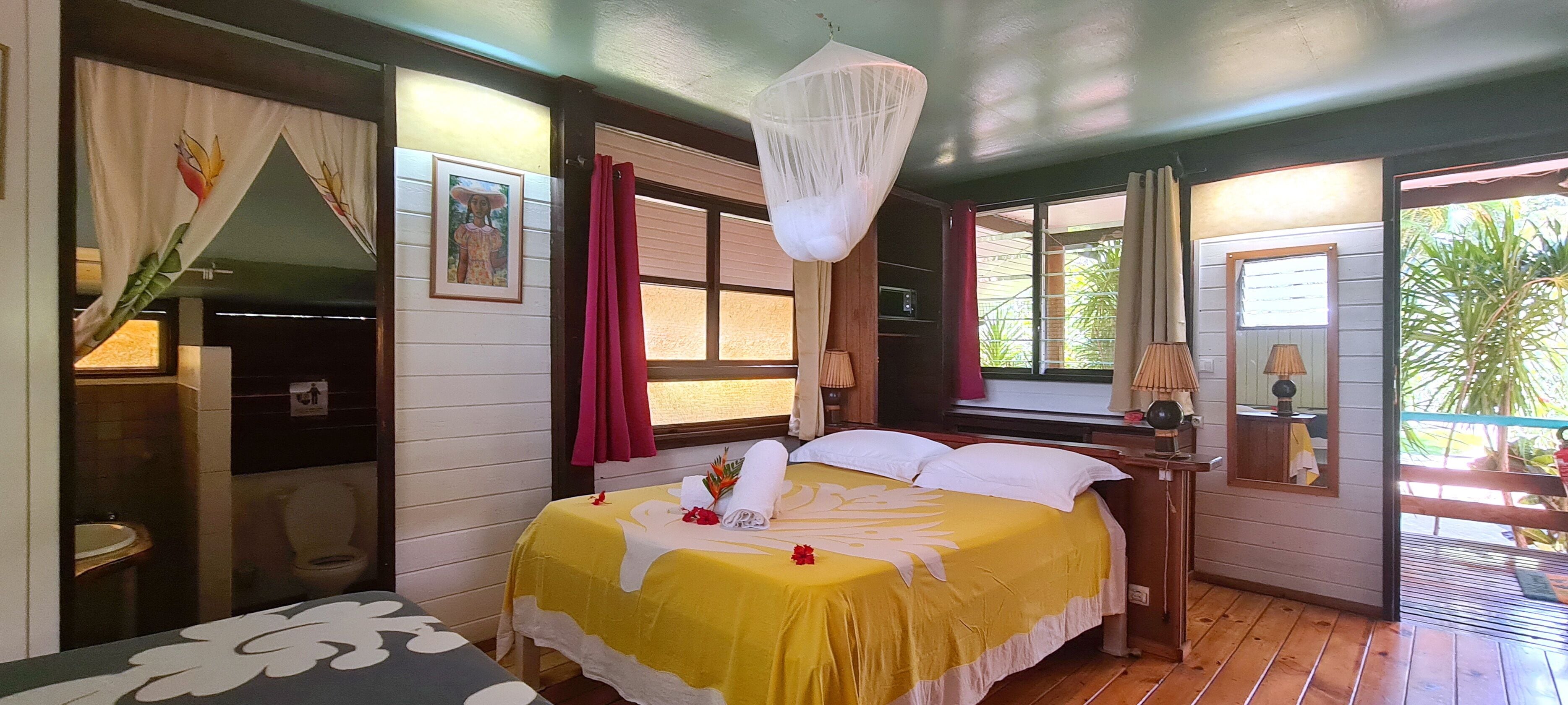 A room with a bed, a nightstand, a window with curtains, a hanging light fixture, and a view of the outdoors.