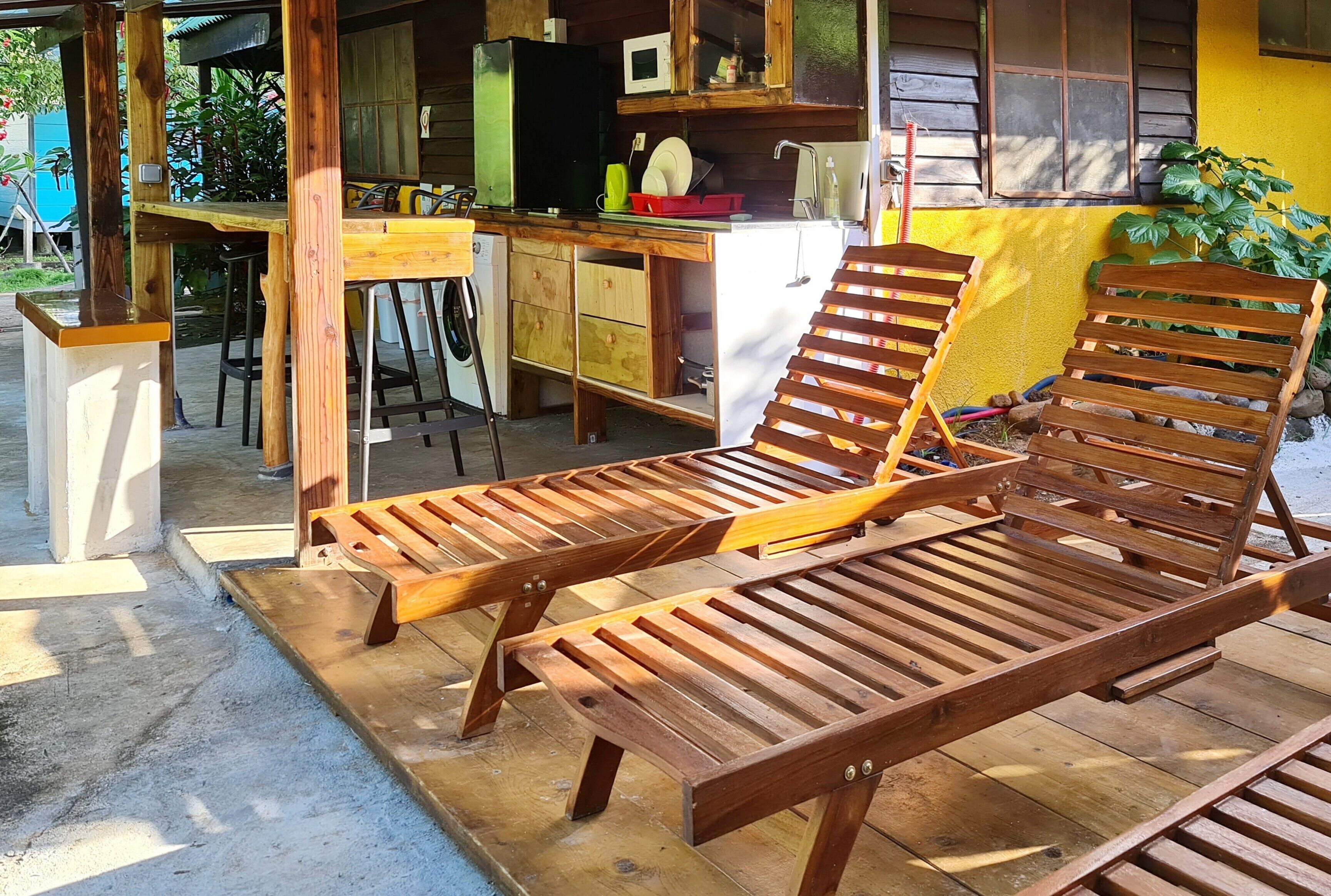 A wooden deck with two lounge chairs and a small kitchen area with a microwave and sink.