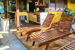 Una terraza de madera con dos sillones de descanso y una pequeña cocina con microondas y lavamanos.