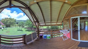 Un espacio exterior techado con cubierta de madera, vistas a un patio césped y un edificio al fondo.