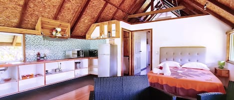 A compact room with a kitchenette, a bed with a floral bedspread, and a small seating area.