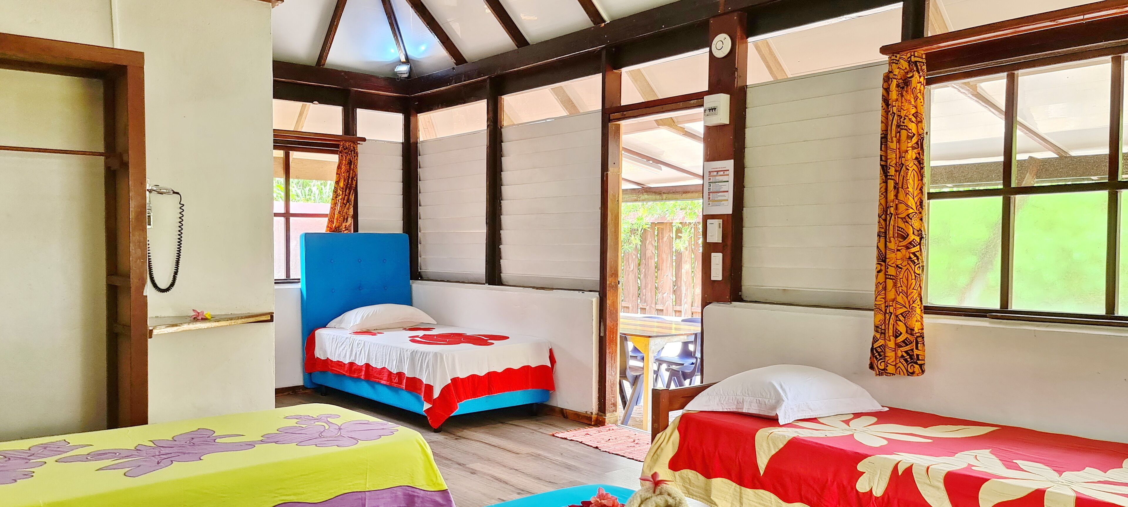 A room with two beds, a wooden ceiling, and a window with curtains.
