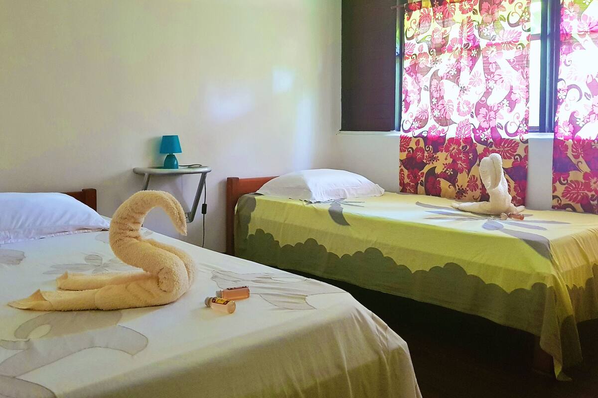 Two beds with floral bedspreads, a lamp on a small table, and a window with a floral curtain.