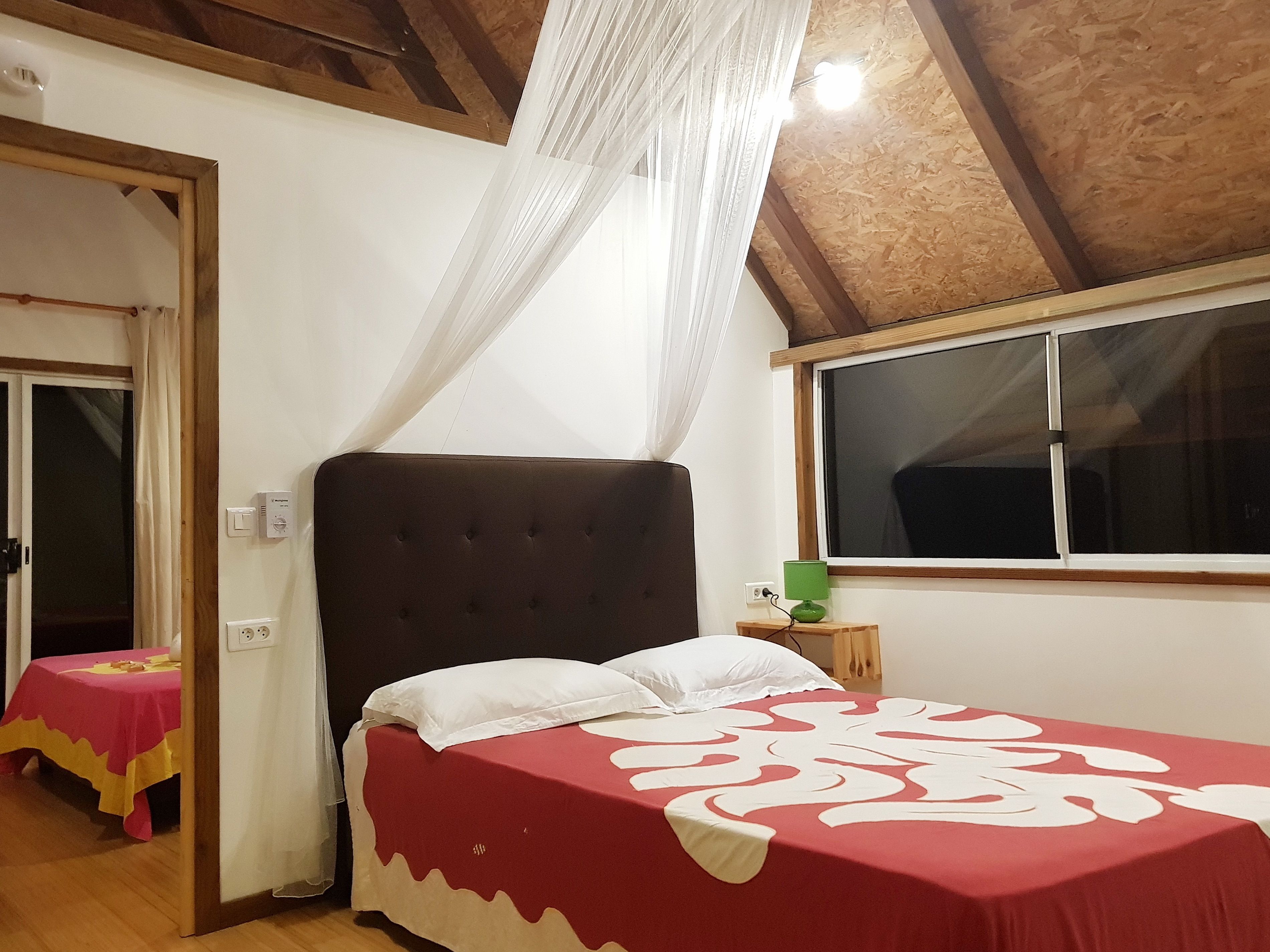 A bedroom with a bed, a window, and a table with a red tablecloth.