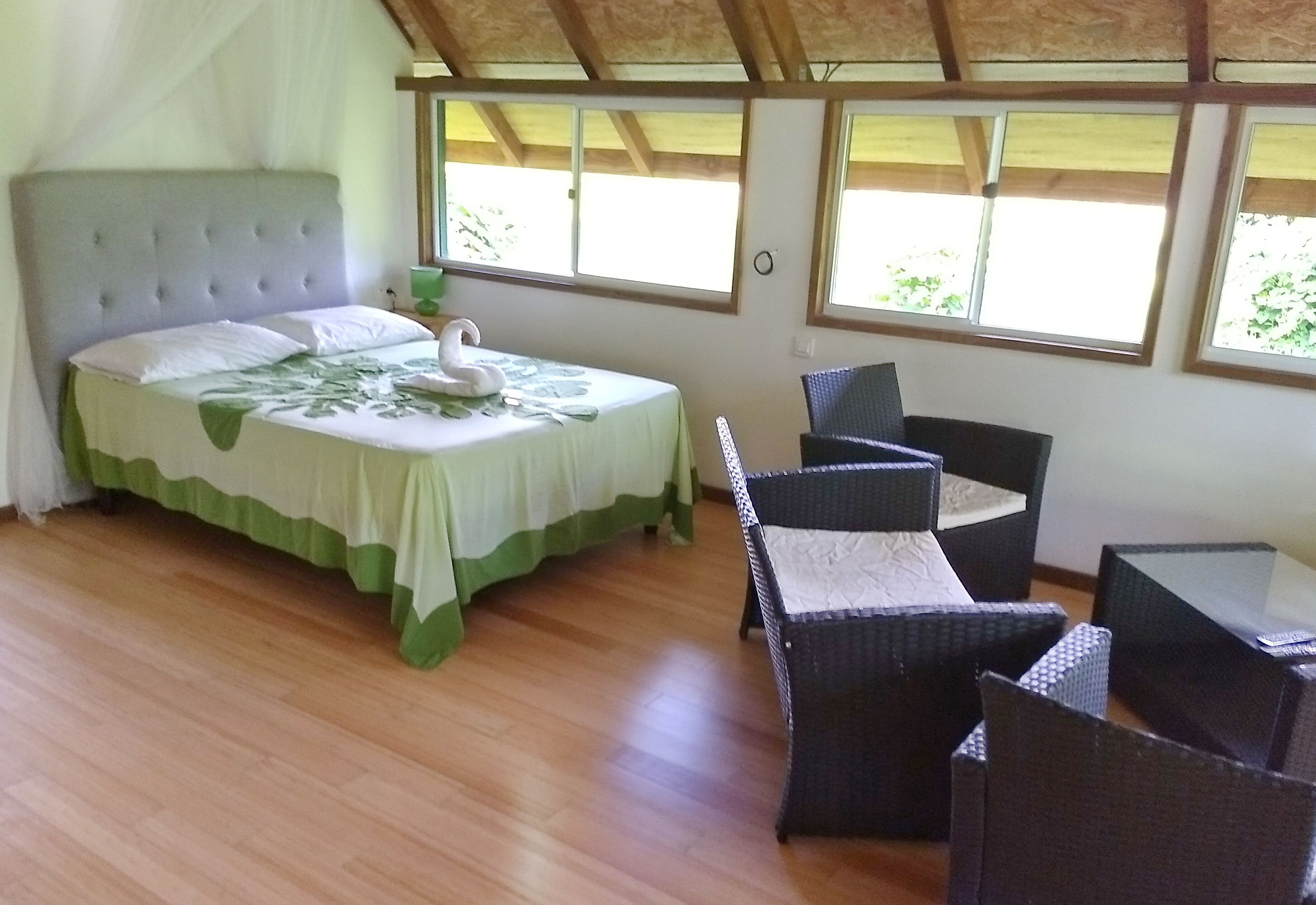 A bedroom with a bed, green and white bedding, a swan pillow, and a window with a view of trees.