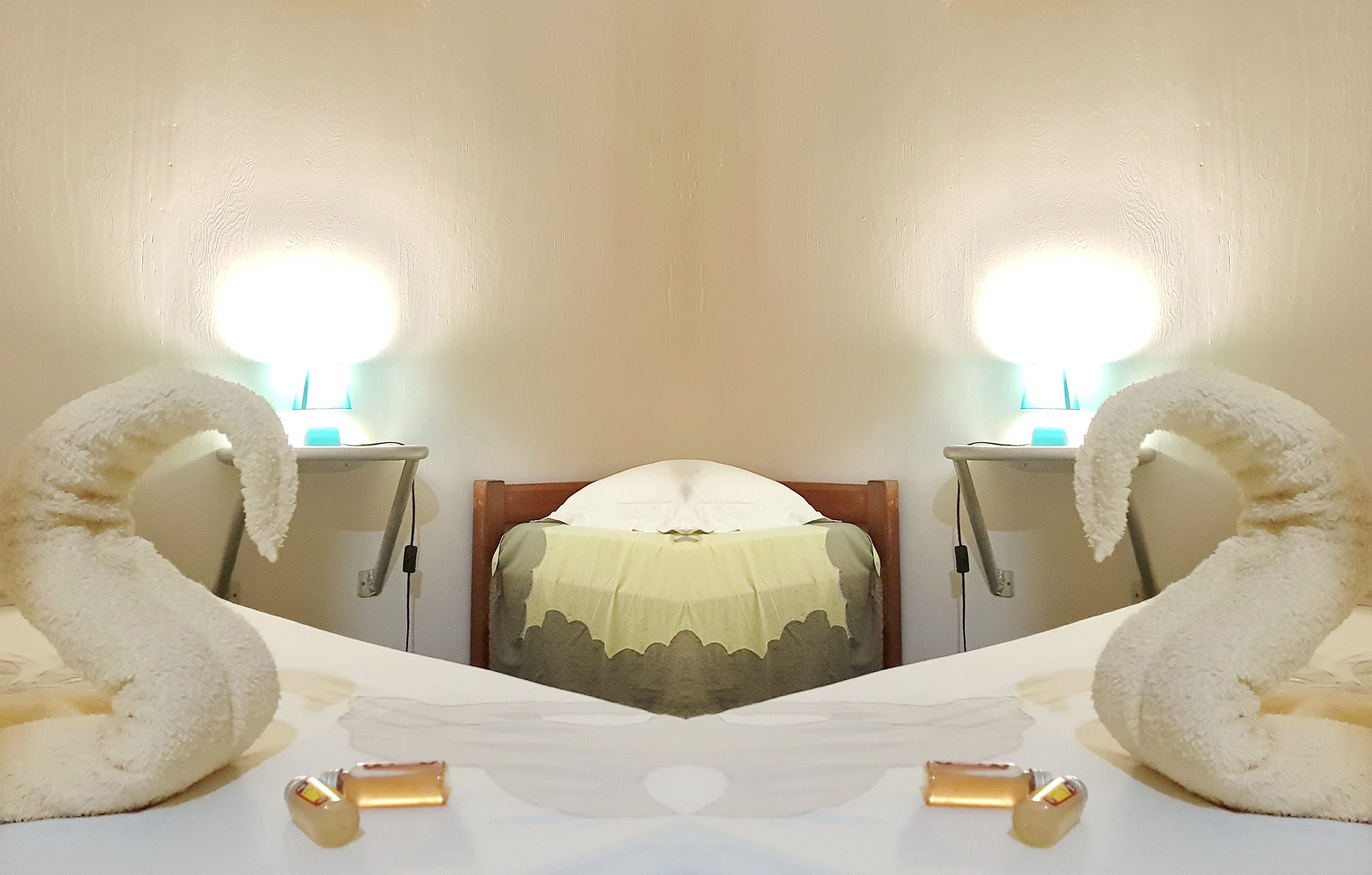 Une pièce aux murs recouverts de miroirs, avec un lit, deux tables de chevet et une lampe.
