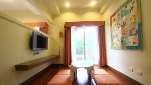 A room with a television on a shelf, a table with a tablecloth, and a colorful quilt on the wall. - Malia Homestay (Hualien City)