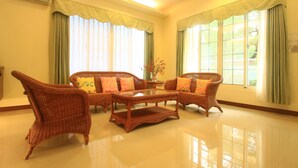 A spacious living room with a large, glossy coffee table, wicker furniture, and large windows with green curtains. - Malia Homestay (Hualien City)