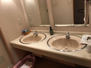 Un baño con dos lavamanos, un espejo y un cesto de basura.