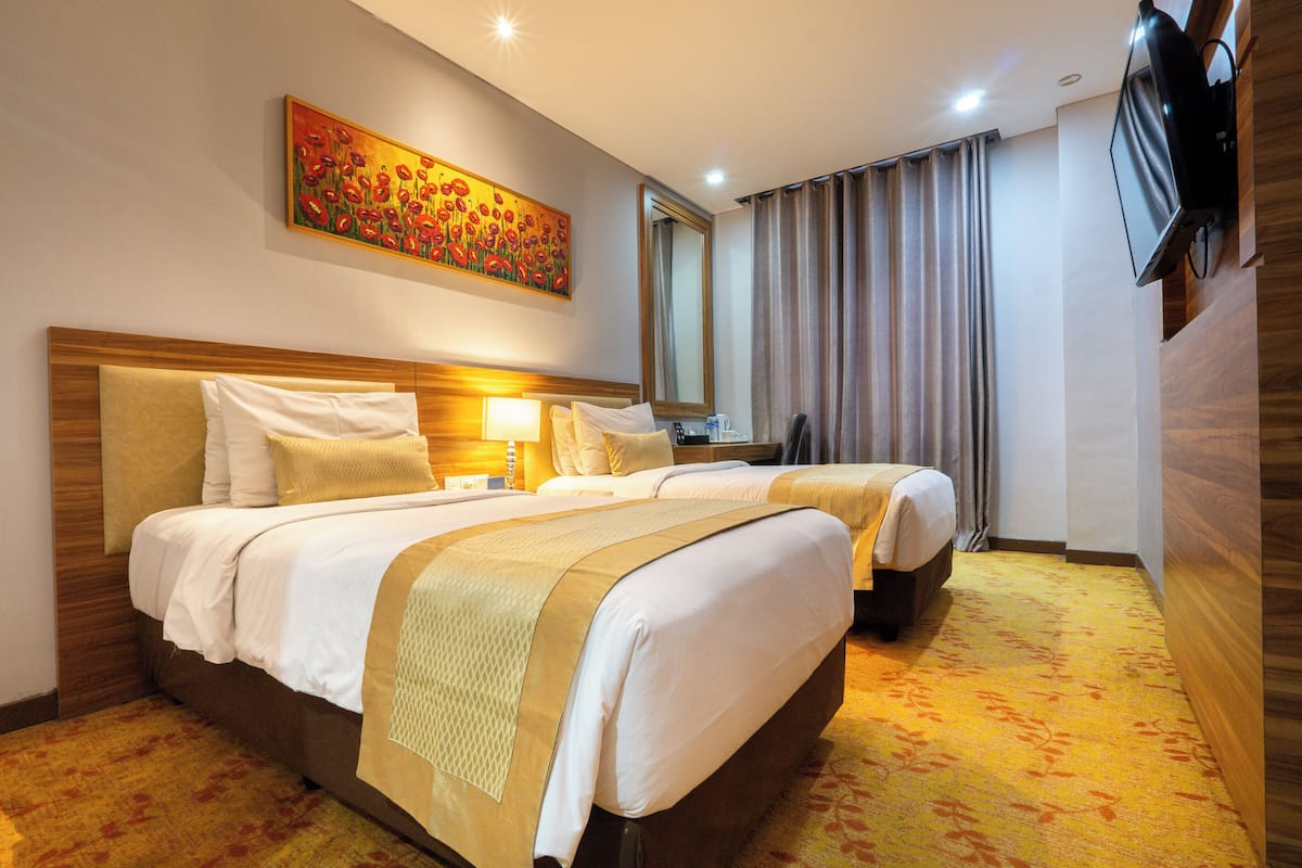 Une chambre d’hôtel avec deux lits, un grand tableau au mur, un téléviseur fixé au mur et un miroir.