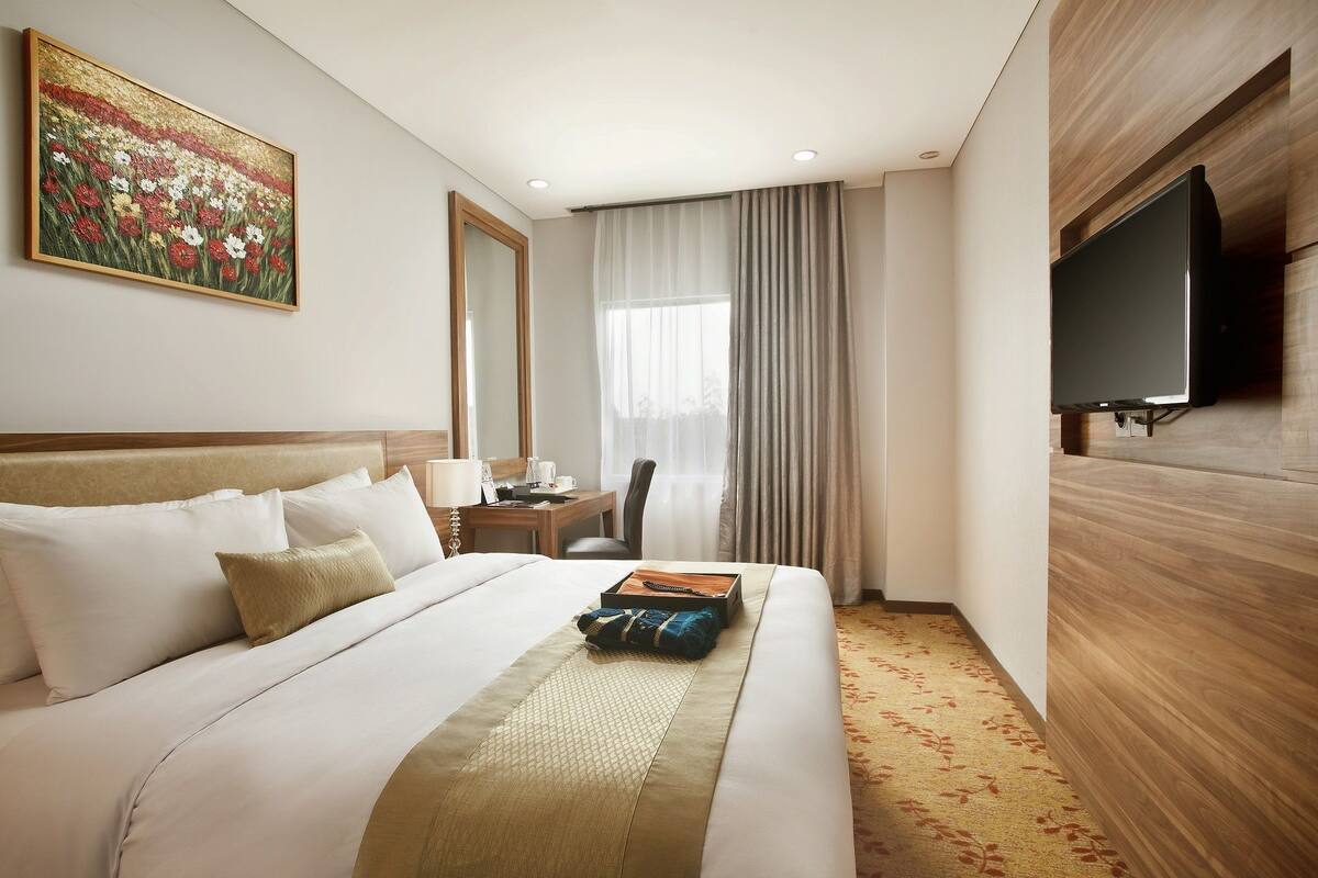 Une chambre d’hôtel avec un grand lit, un bureau avec une chaise, une télévision et un tableau au mur.