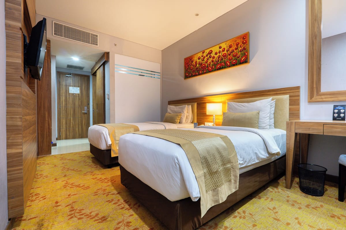 Une chambre d’hôtel avec deux lits, un téléviseur fixé au mur, un tableau au-dessus des lits et un bureau avec une chaise.