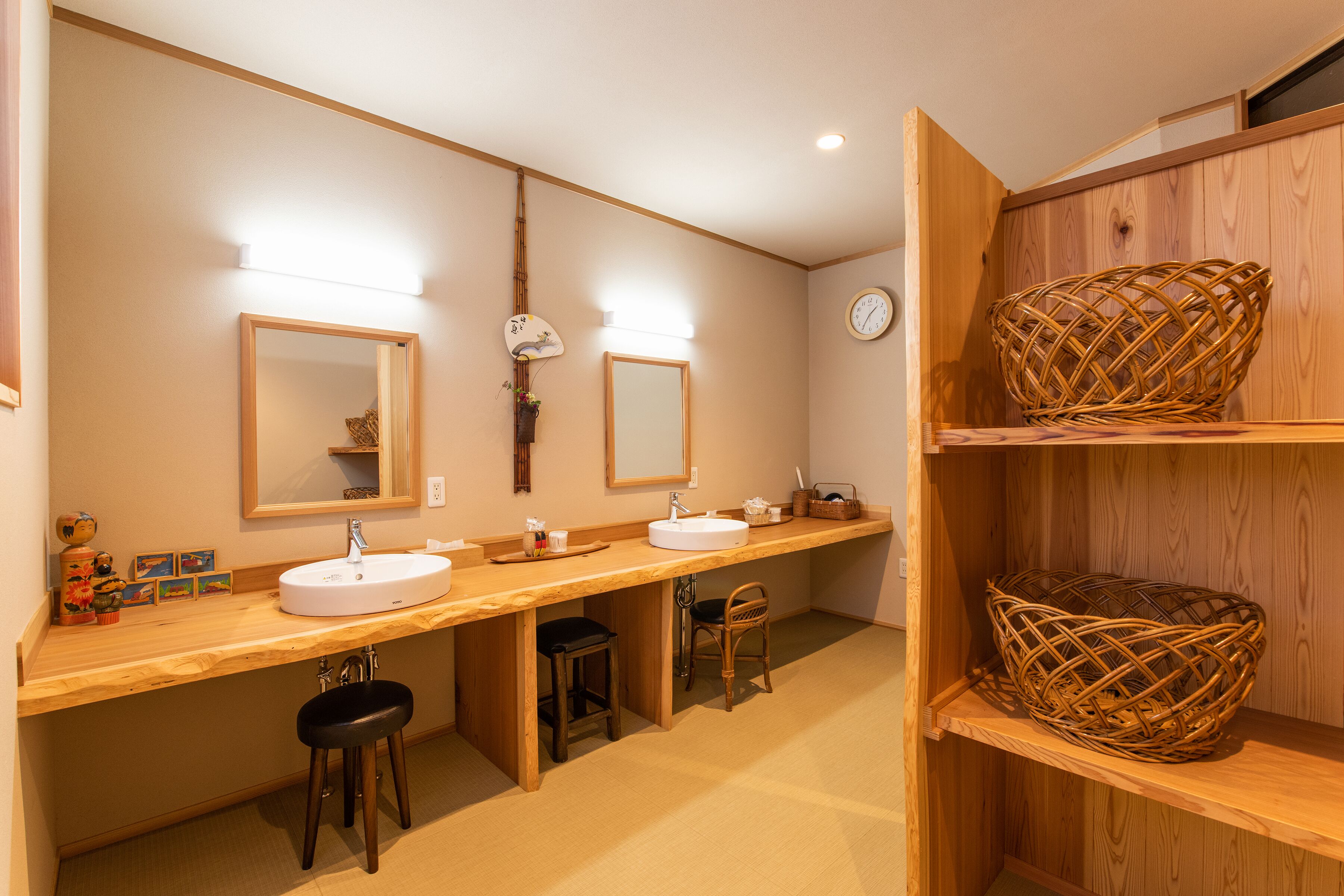 A bathroom with two sinks, mirrors, stools, and a shelf with a woven basket.