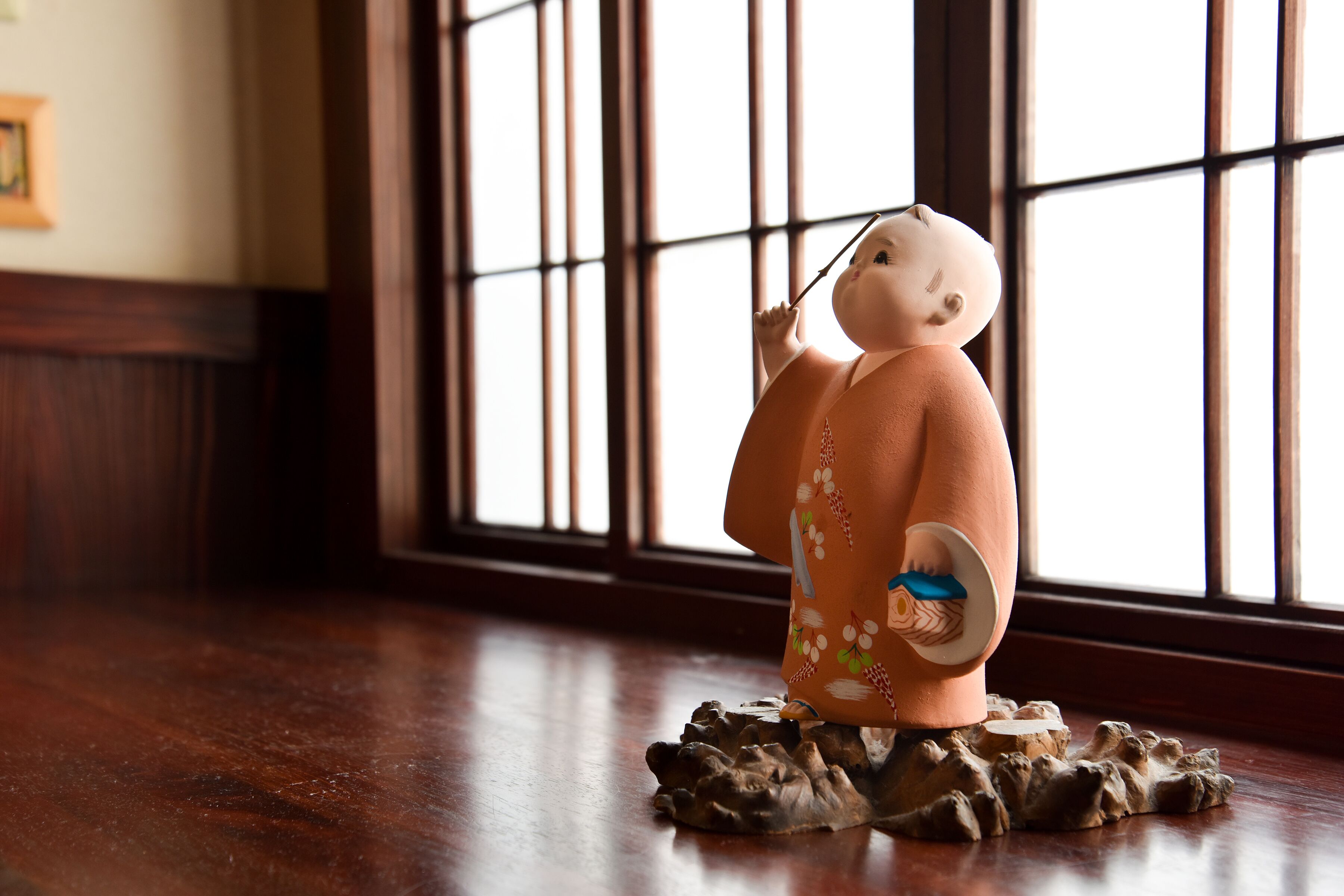 A figurine of a person on a rock base, positioned in front of a window with vertical bars.