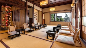 Una habitación japonesa tradicional con suelo de tatami, mobiliario de madera y vistas a una estatua a través de una ventana.