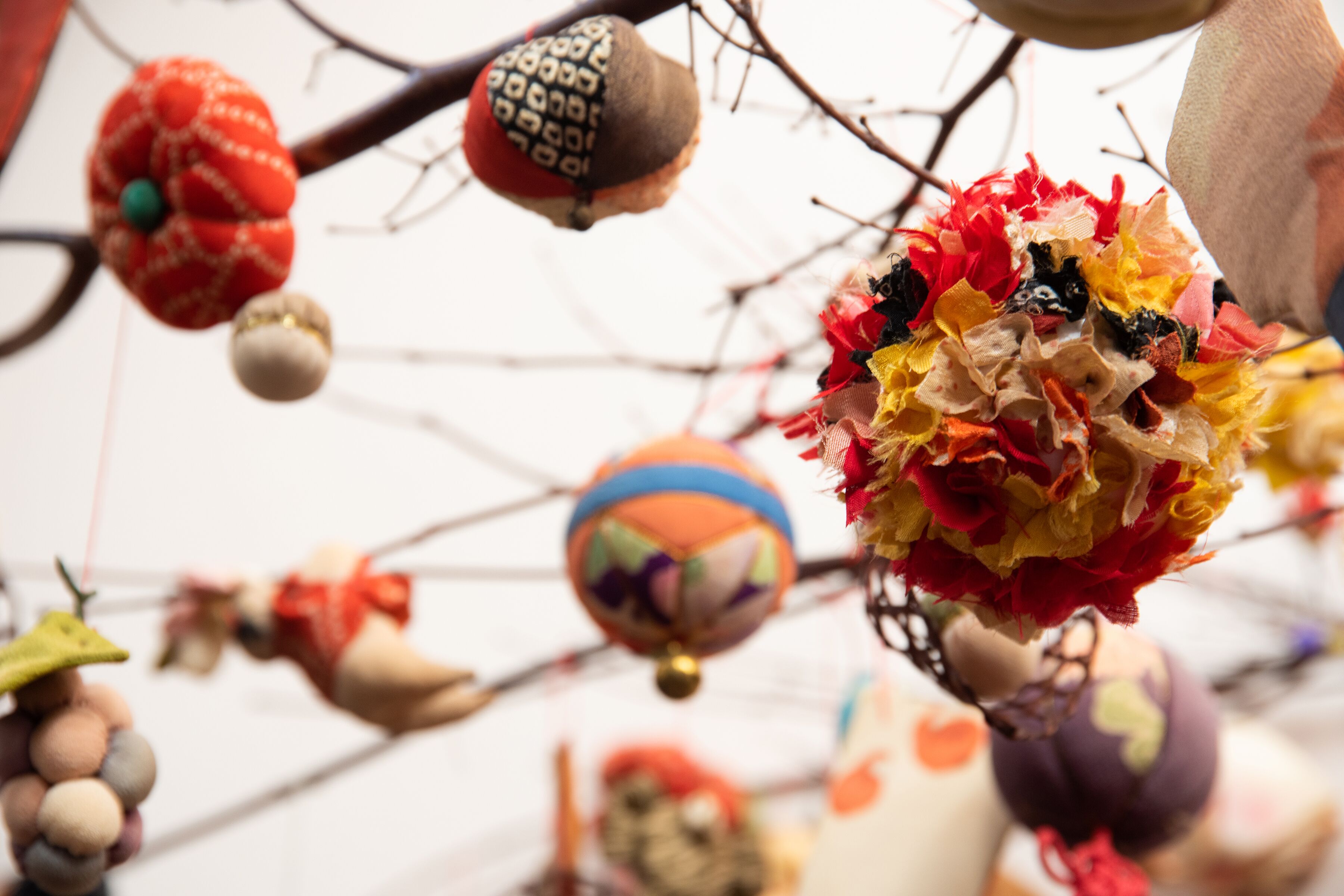 Verschiedene hängende Dekorationen, darunter ein rot-grüner Schmuck, ein gemustertes braunes Ornament und eine farbenfrohe Kugel.