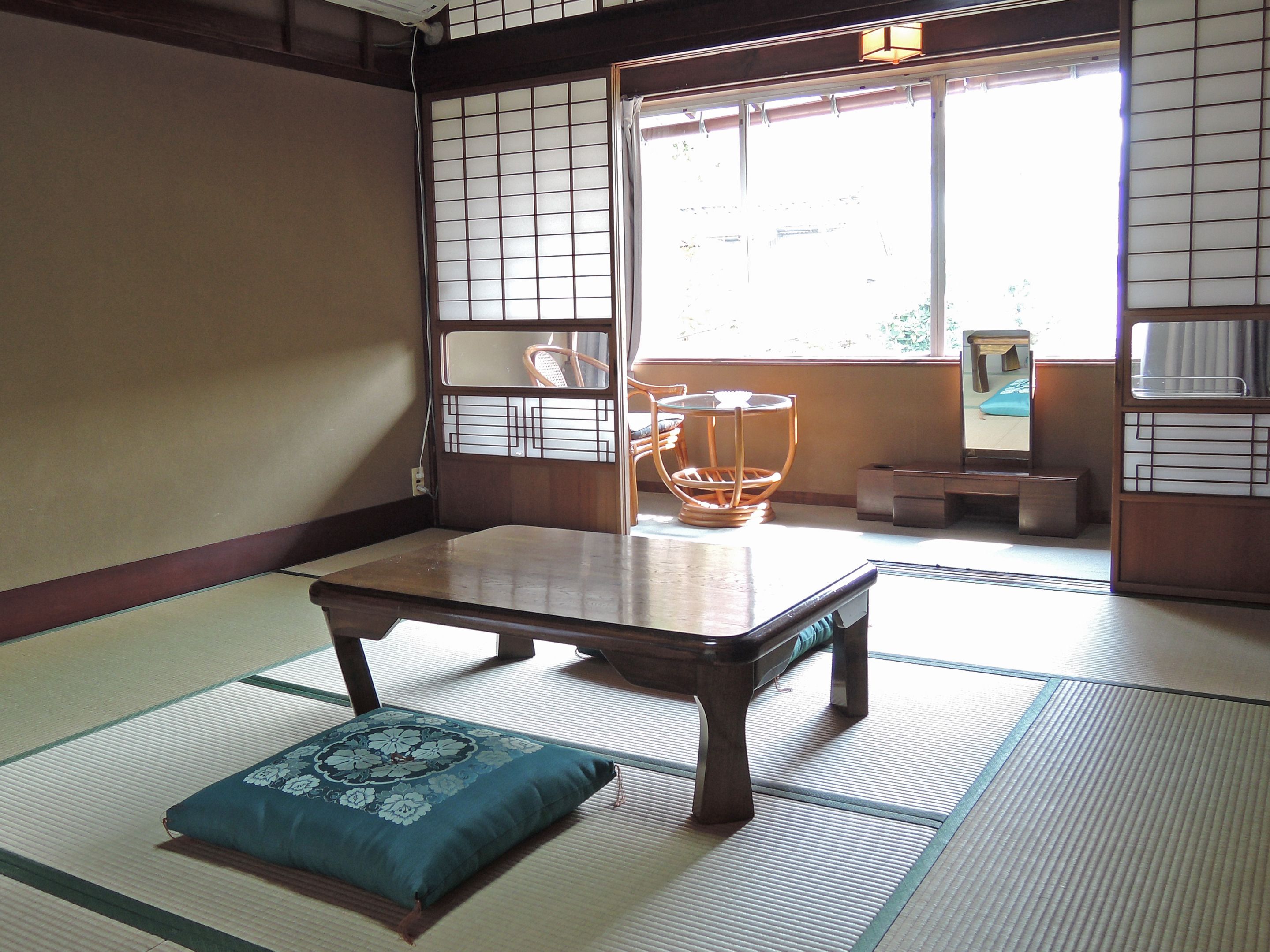 A tatami mat room with a low wooden table, a cushion, and a window with a view.