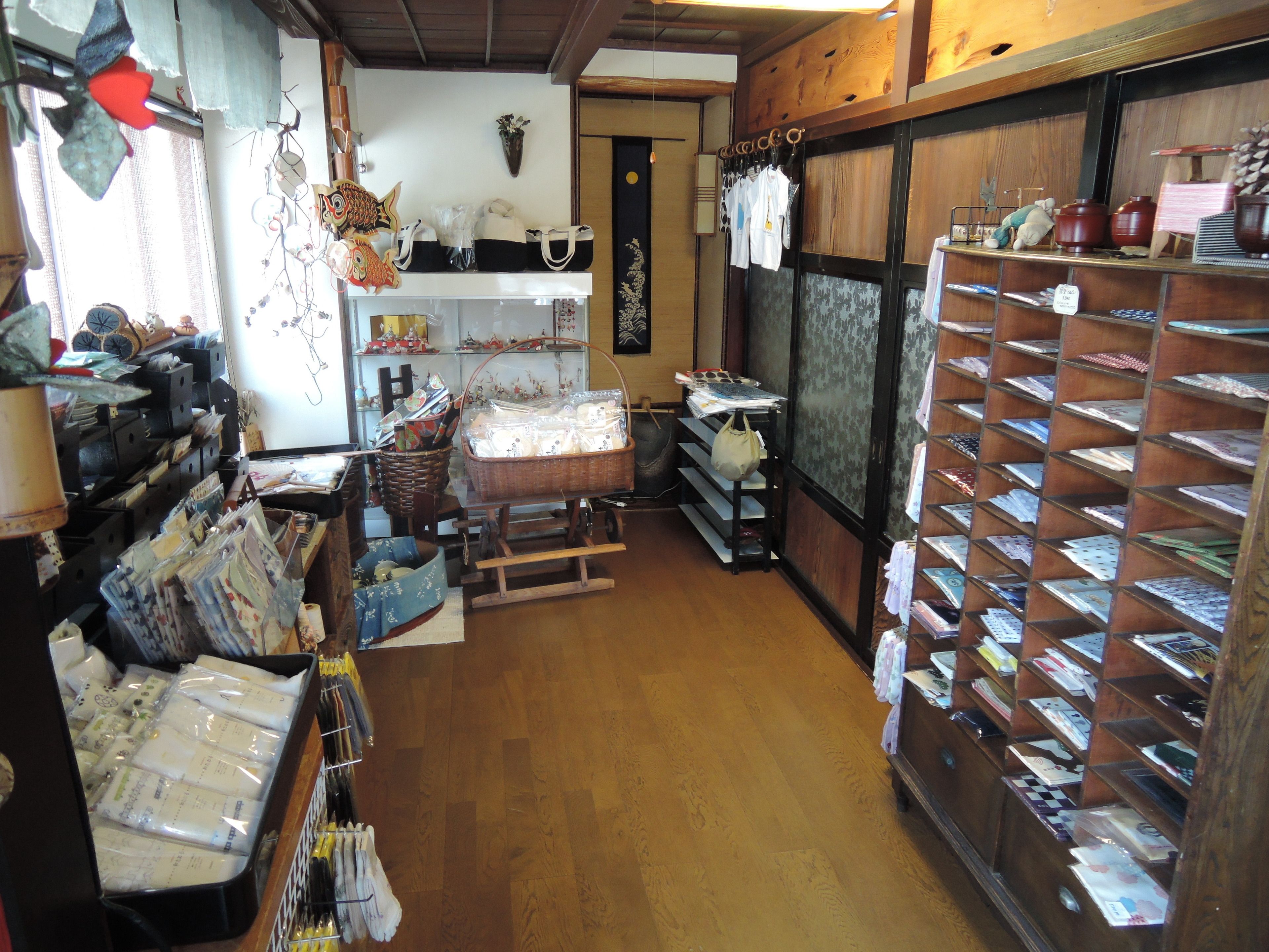 A store with shelves of various items, a wooden floor, and a window with curtains.