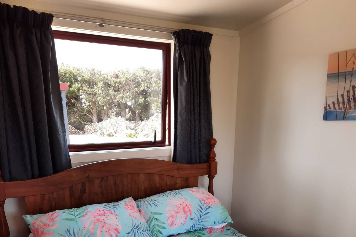 Ein Schlafzimmer mit einem Bettgestell aus Holz, blumigem Bettzeug und einem Fenster mit Vorhängen.