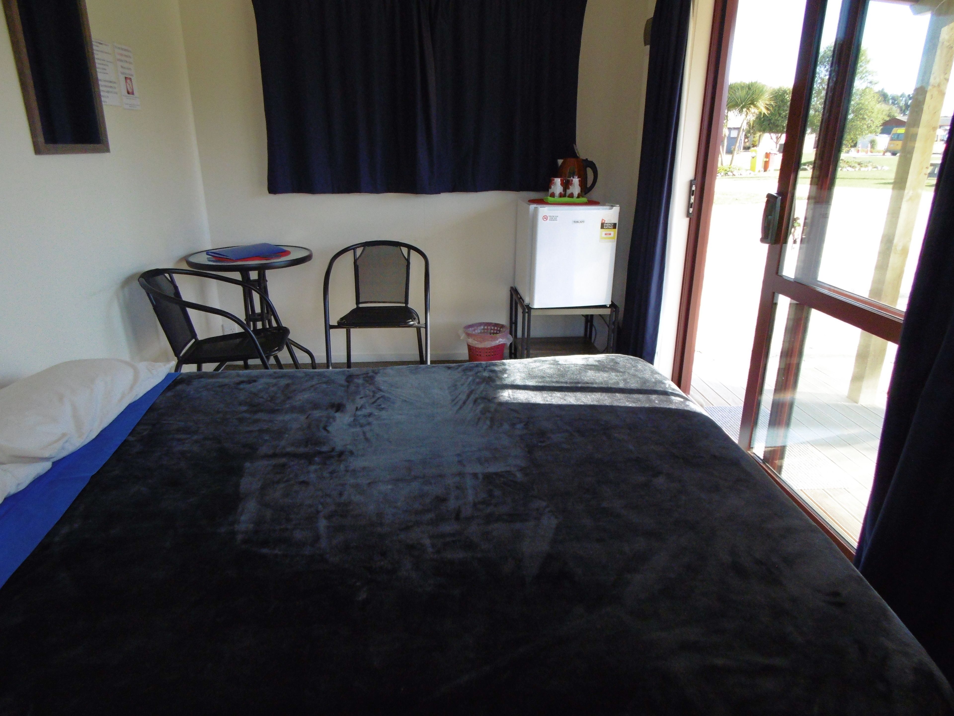 Habitació amb llit, dues cadires, taula petita, pissarra i finestra amb cortines.