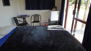 Habitació amb llit, dues cadires, taula petita, pissarra i finestra amb cortines.