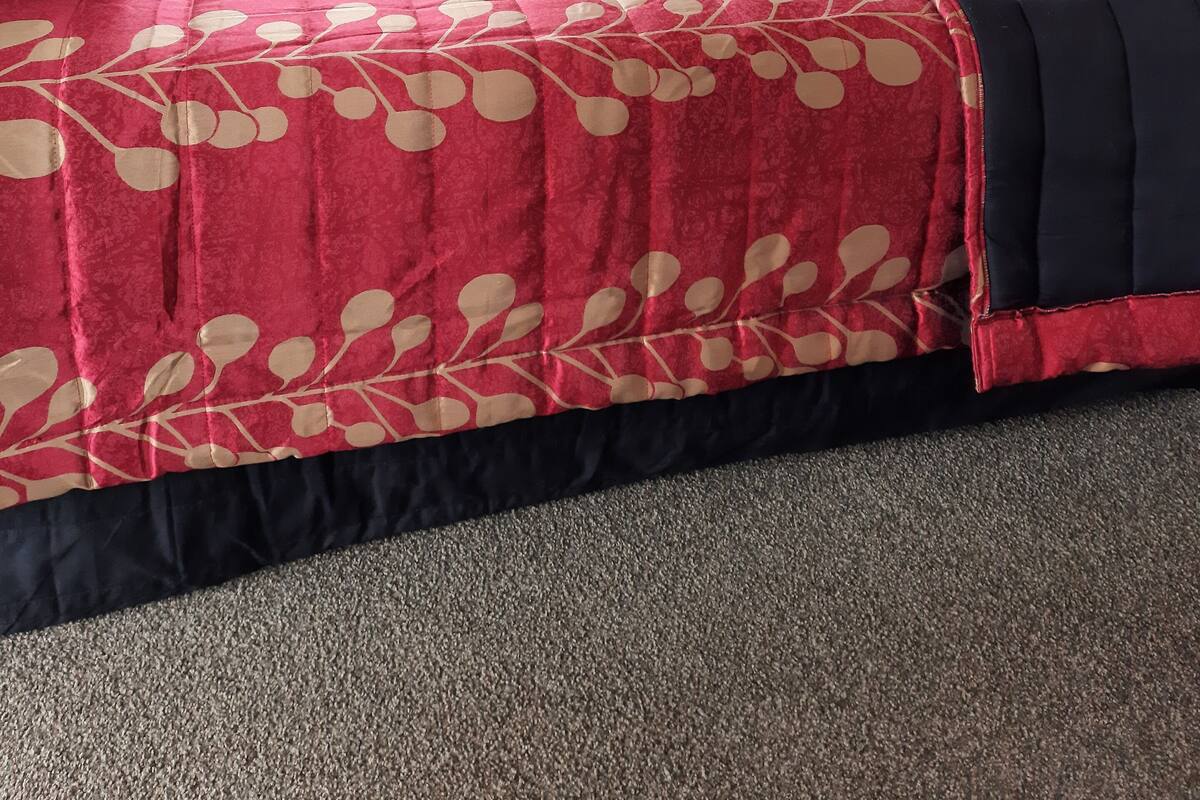 Ein Bett mit roter und schwarzer Bettdecke, weißen Kissen und einem Fenster mit Vorhängen.