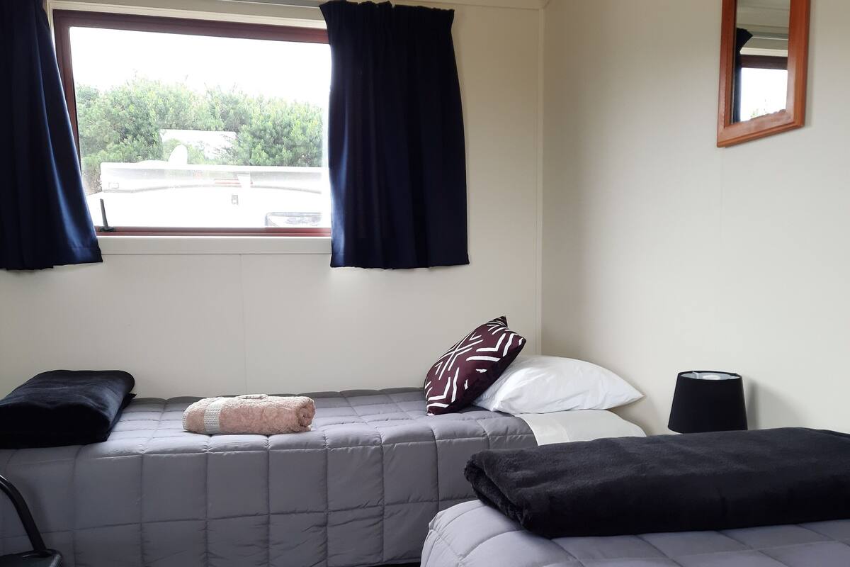 Ein Schlafzimmer mit zwei Betten, einem Fenster mit Vorhängen, einem Nachttisch und einem Sessel.