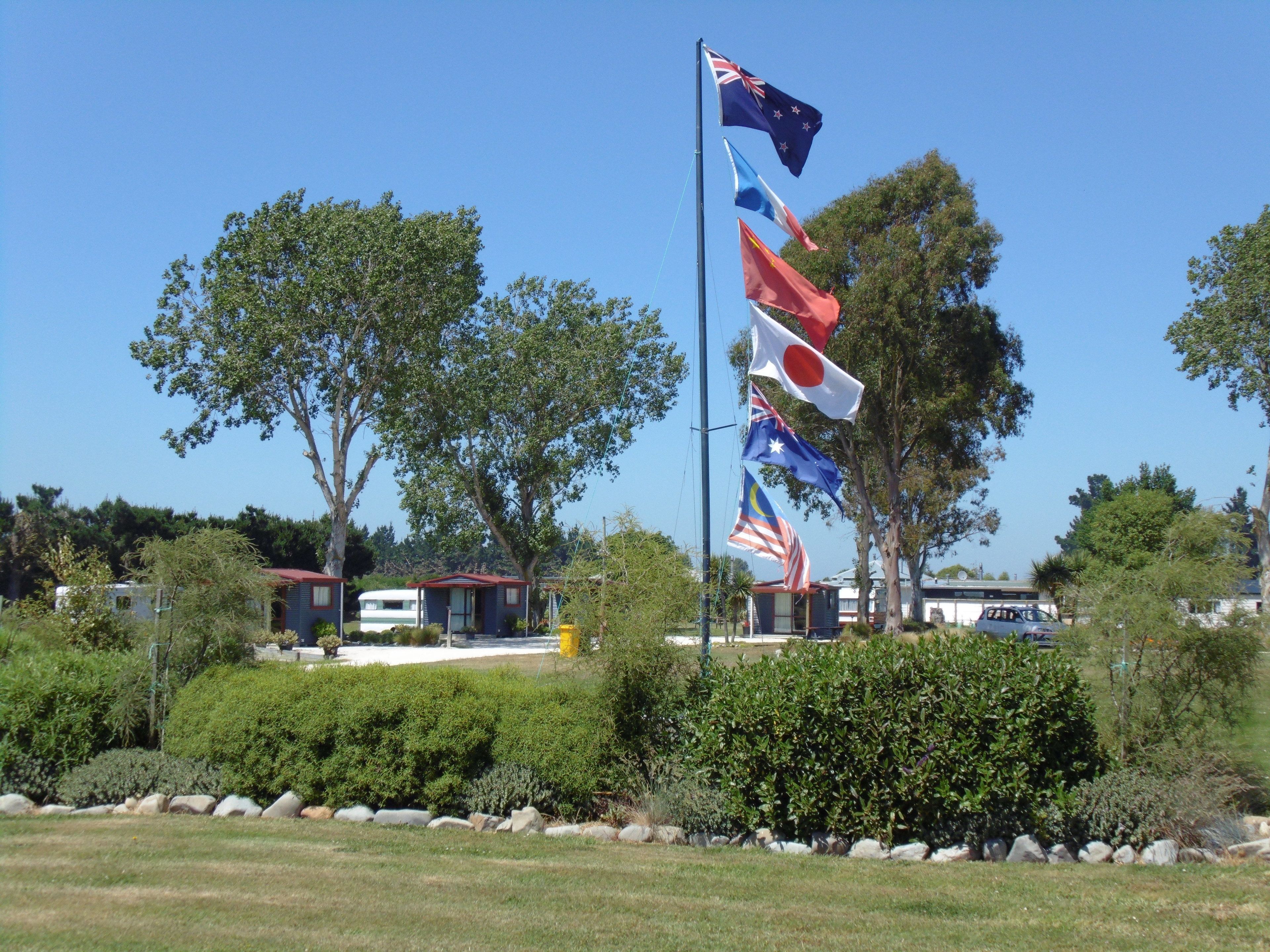 A flagpole with multiple national flags, surrounded by greenery and a clear sky.