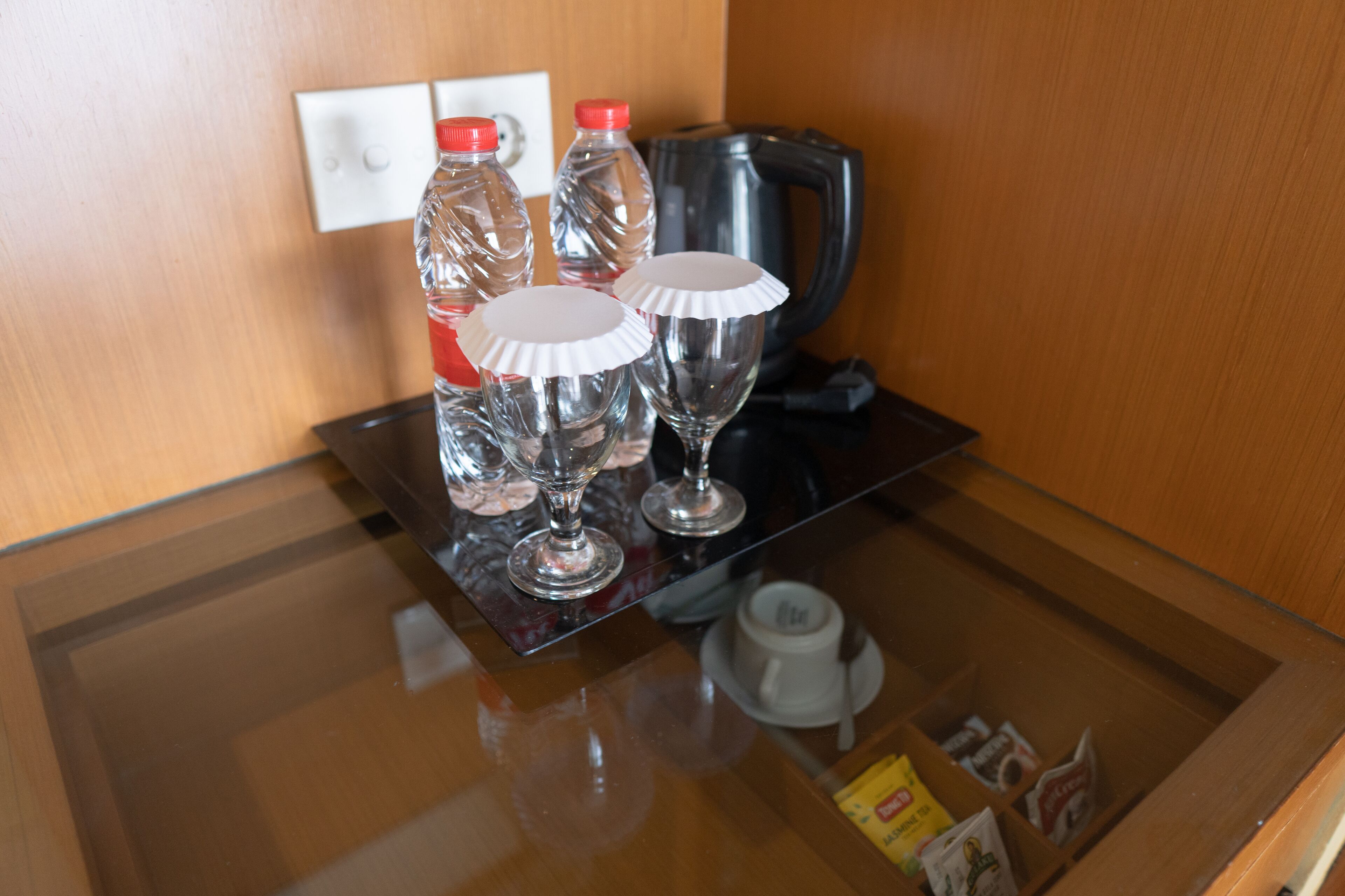 A glass-top table with a coffee maker, two bottles, two glasses, and a small cup.