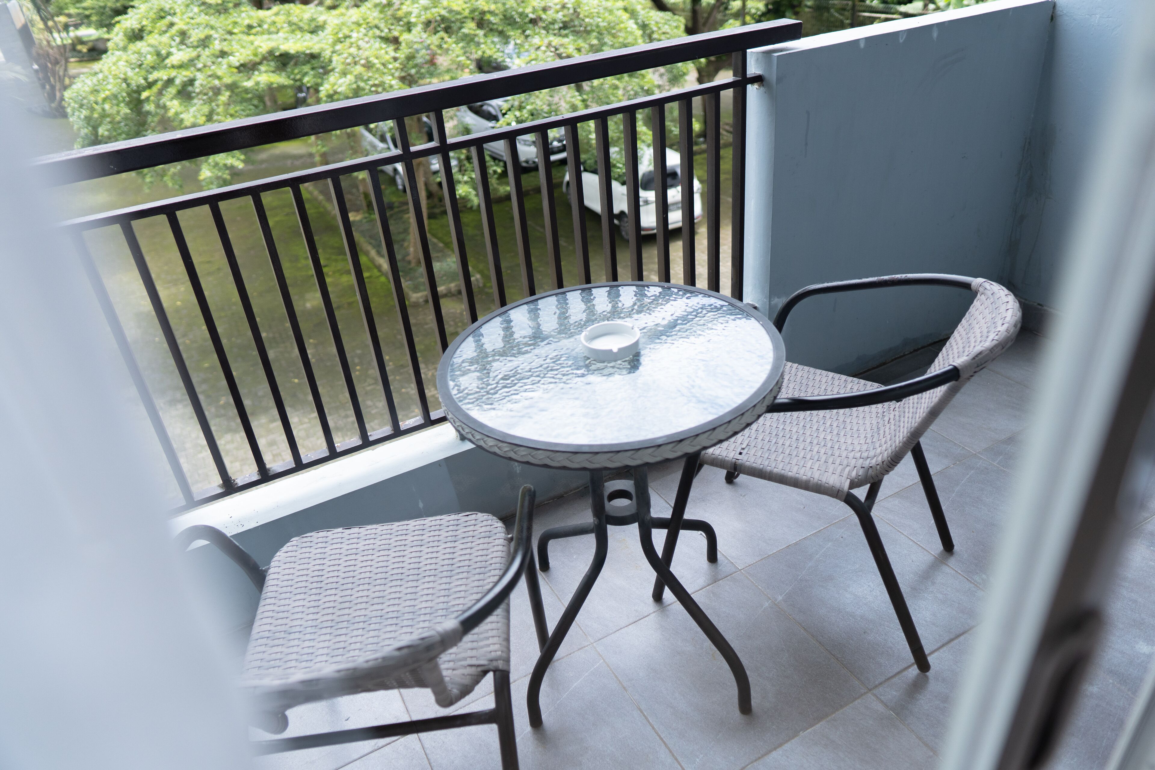 A balcony with a round glass table and two wicker chairs.