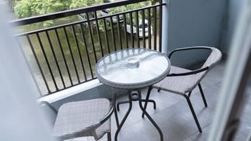 A balcony with a round glass table and two wicker chairs.