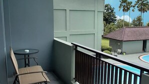 Un balcón con mesa y silla, una piscina y vistas a palmeras y edificios.