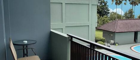 Un balcón con mesa y silla, una piscina y vistas a palmeras y edificios.