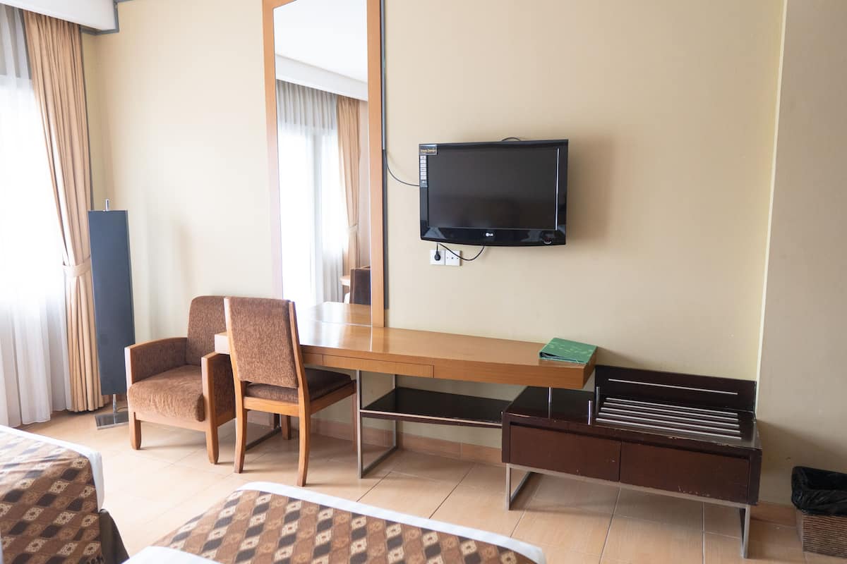 A hotel room with a wooden desk, two chairs, a television mounted on the wall, and a small cabinet.