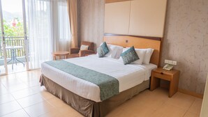 Habitación de hotel con una cama grande, dos mesitas de noche, una silla y un balcón con vistas.
