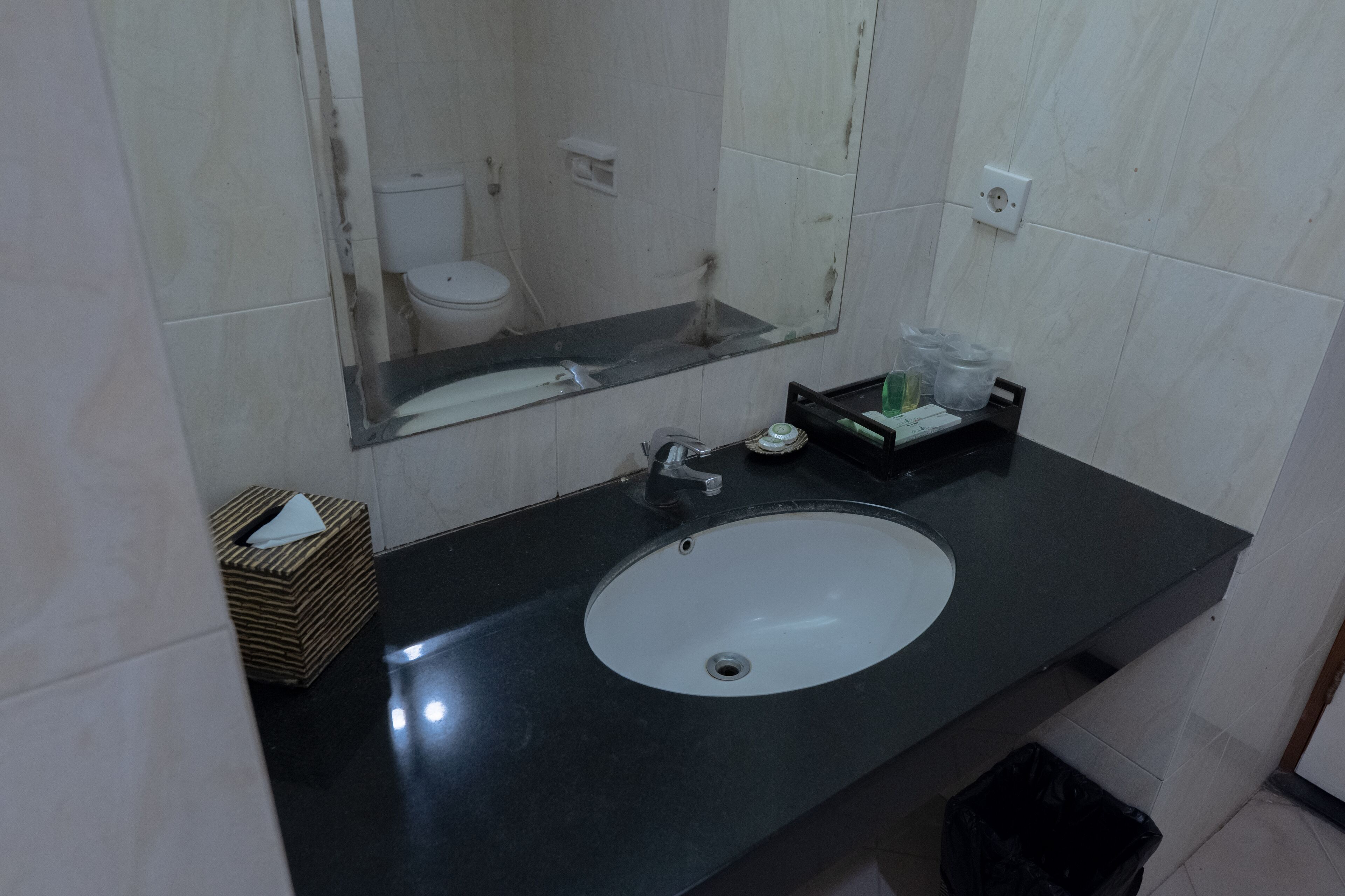 A bathroom with a black countertop, a white sink, a mirror, and a toilet.