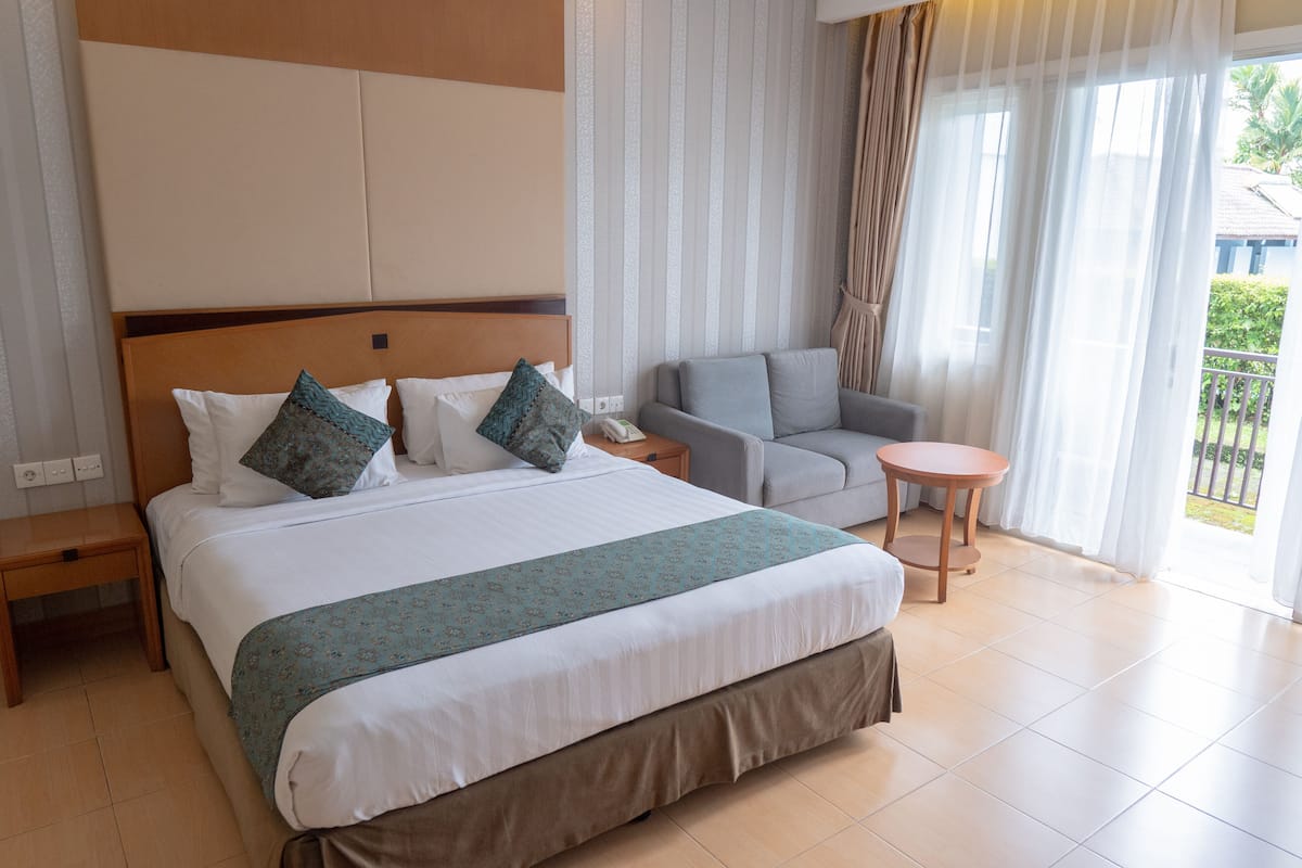 A hotel room with a large bed, a sofa, a small table, and a view of the outdoors.