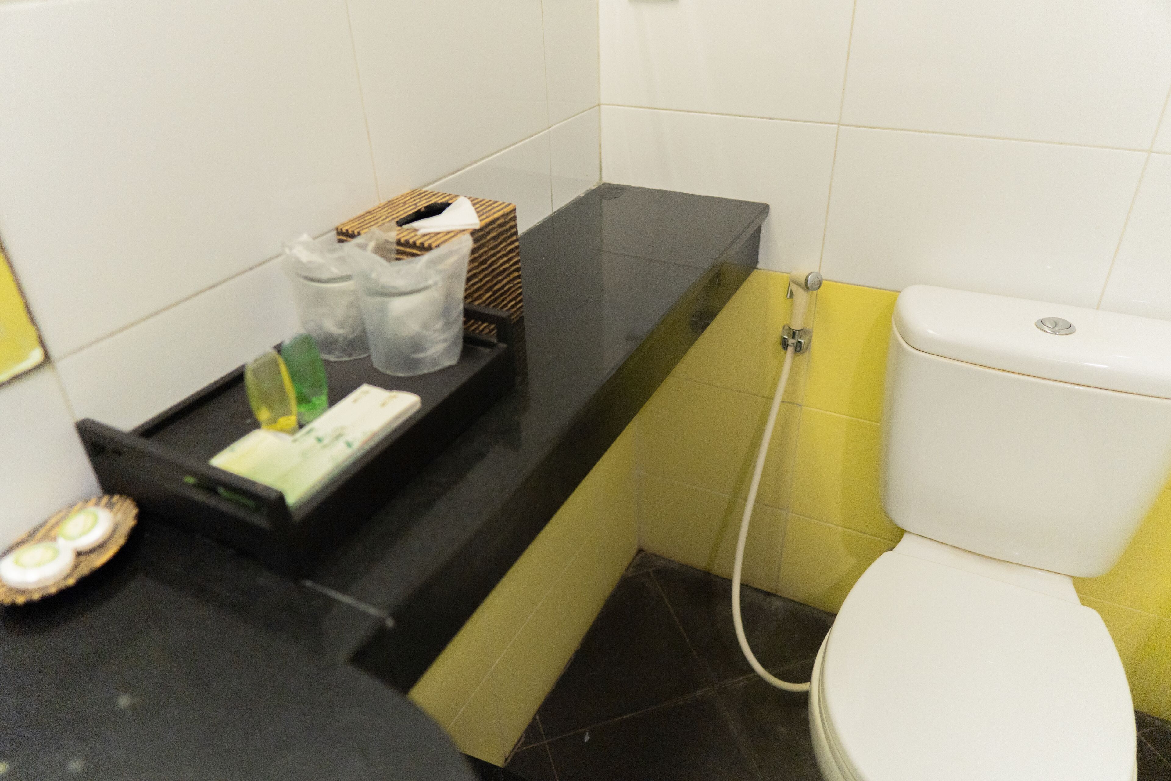 Un baño con encimera negra, inodoro blanco y pared amarilla.