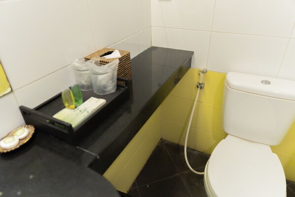 A bathroom with a black countertop, a white toilet, and a yellow wall. - Green Valley Resort (Baturaden)